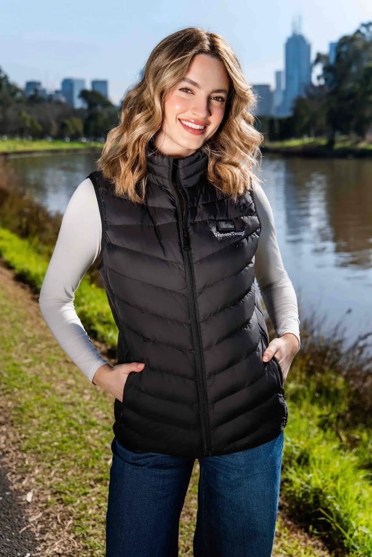 Smiling woman wearing a black VentureTemp° heated vest outdoors near a riverside in Melbourne city.